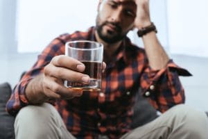 A man holds a glass and wonders if he should enroll in an alcohol addiction treatment program
