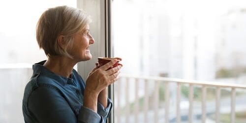 6589 A woman holds a cup of coffee as she looks out a window and thinks about 5 ways to become more emotionally intelligent in recovery