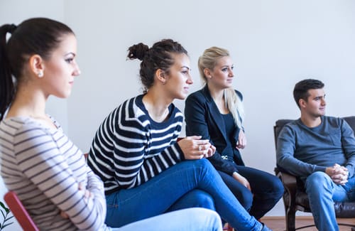 A group of people listen to a speaker talk about the benefits of group therapy