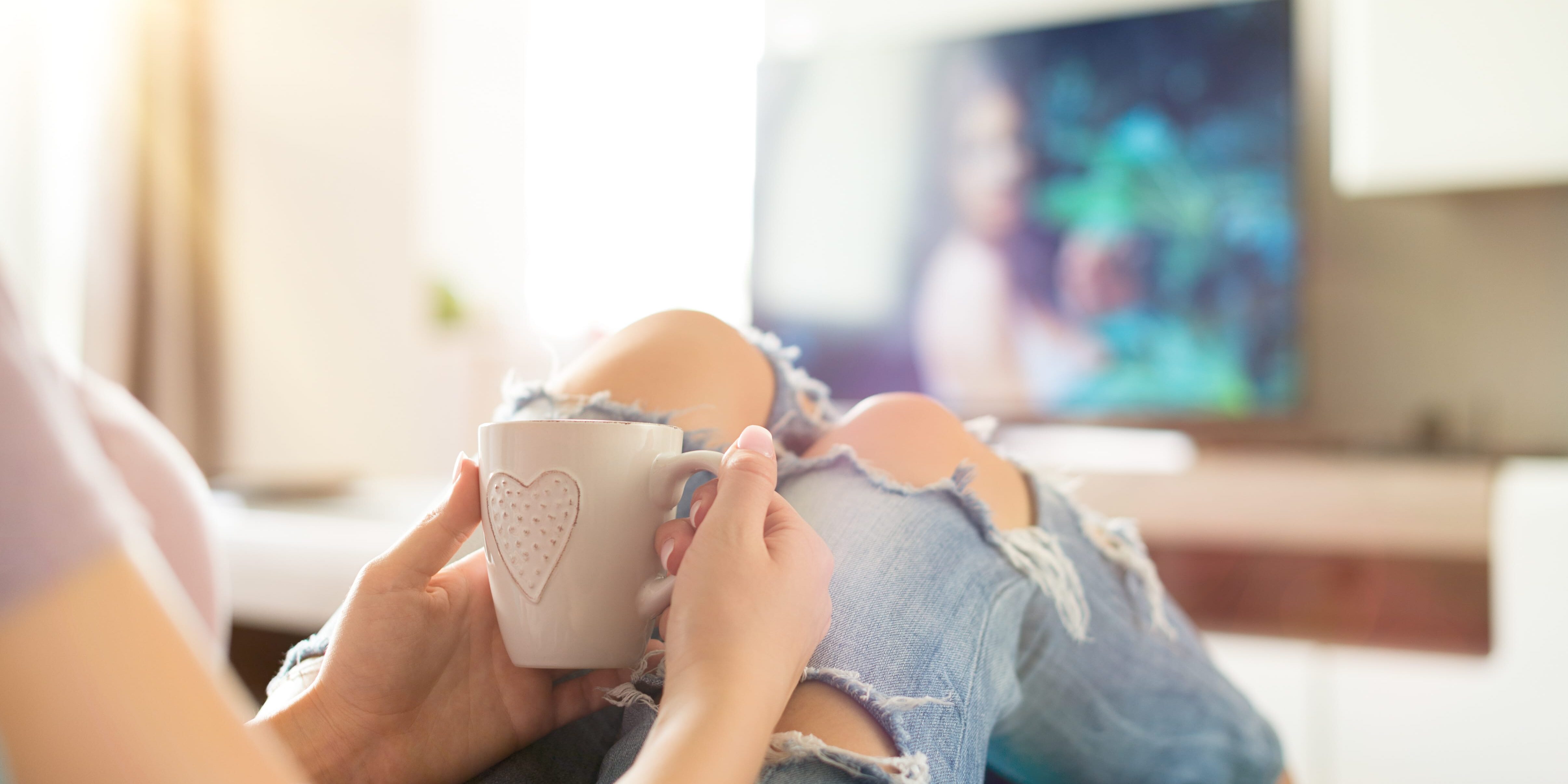 Young woman relaxing on the sofa at home, watching tv and enjoying coffee as she wonders, "Do anti-drug commercials work?"