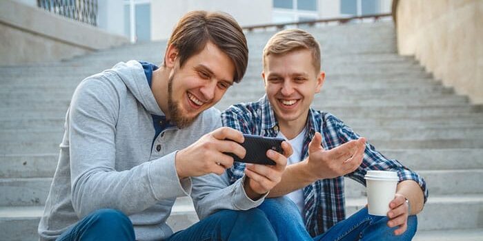 How-ADHD-Can-Lead-to-Addiction A man and his friend watch a video on his phone about how ADHD can lead to addiction