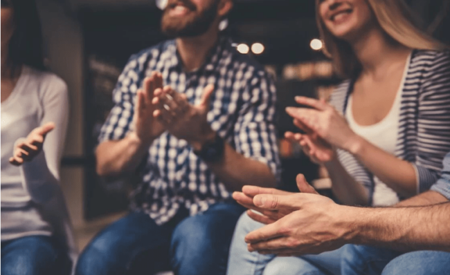 A group of people clap as they listen to a person talk about the topic "Does it really matter how we talk about addiction?"