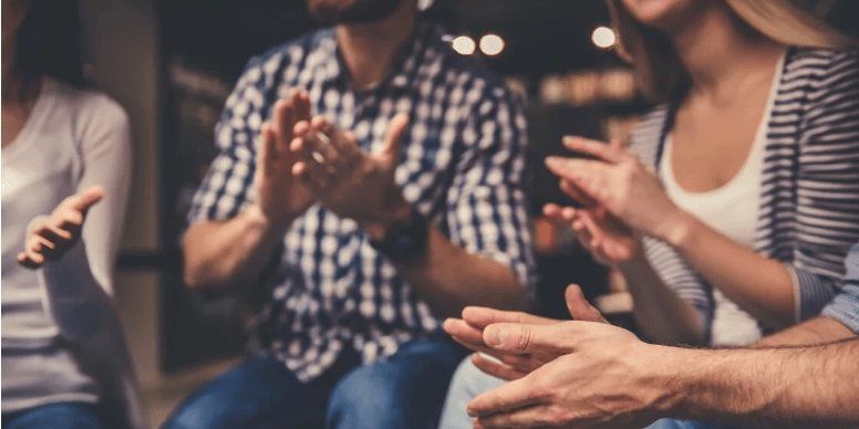 A group of people clap as they listen to a person talk about the topic "Does it really matter how we talk about addiction?"