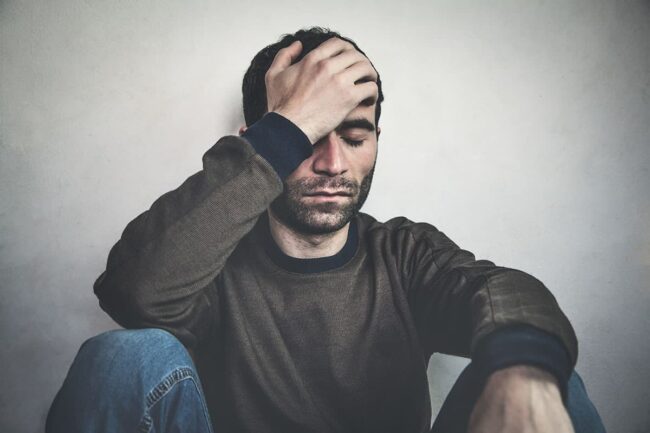 alcohol withdrawal symptoms A man sits against a wall with his hand on his head, wondering about alcohol withdrawal symptoms