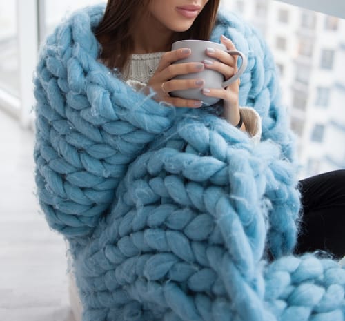 A woman wraps herself in a blanket and drinks hot cocoa as she thinks about 4 winter challenges for people recovering from addiction