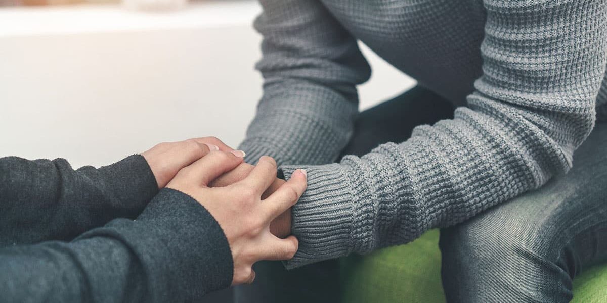 A therapist holds his patient's hands between his own as they talk about the alcohol detox timeline and how long is alcohol detox