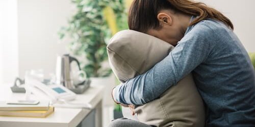 A woman hugs a pillow to her face as she thinks about how deep brain stimulation may relieve depression symptoms