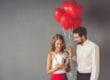 A man holds a bunch of balloons for his girlfriend as she reads his card, while they work on celebrating Valentine's Day sober