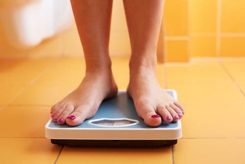 A woman steps on a scale and wonders how are depression and obesity related