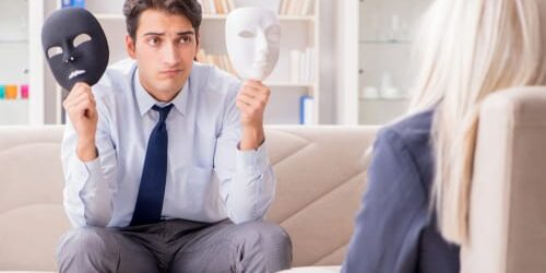 a man holds up a black and white mask and asks his therapist what causes mood swings in people with bipolar disorder