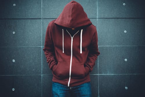 a man leans against the wall with a hood over his head and thinks about common misconceptions about schizophrenia