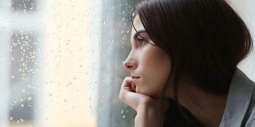a woman stares out a window on a rainy day and wonders how to deal with seasonal affective disorder