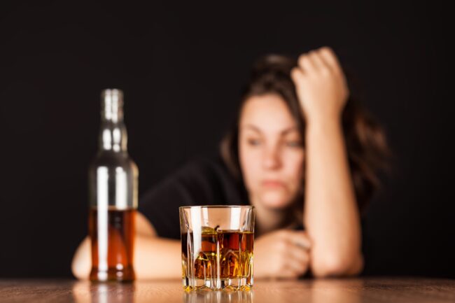 Alcoholism, alcohol, alcoholic. a woman stares at a bottle and wonders about the 4 stages of alcoholism