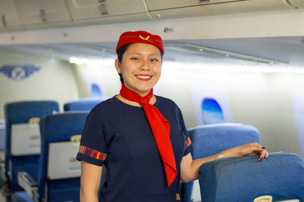 A flight attendant smiling in the aisle of a plane