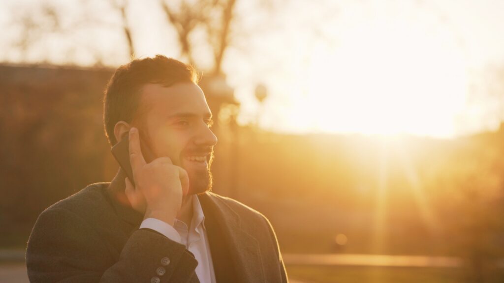 A man talking on the phone with the sun in the background